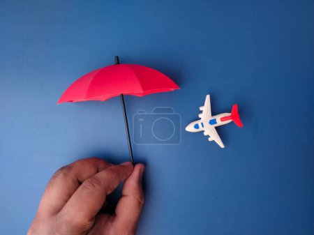 Photo for Hand holding red umbrella covered airplane on a blue background - Royalty Free Image