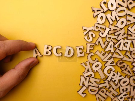 Téléchargez les photos : La main d'une personne arrange des lettres en bois dans l'ordre de ABCDE sur un fond jaune - en image libre de droit