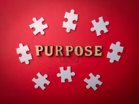 Top view wooden word and white puzzle with the word PURPOSE on a red background