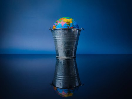 Earth globe in a steel bucket with reflection on a black acrylic board