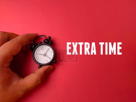 Téléchargez les photos : Réveil main tenant le mot EXTRA TIME sur fond rouge - en image libre de droit