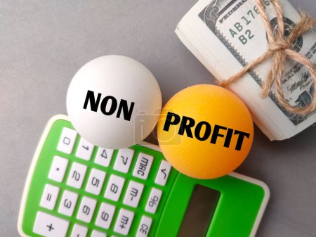 Taschenrechner, Banknoten und Tischtennisball mit Wort NICHT PROFIT auf grauem Hintergrund.
