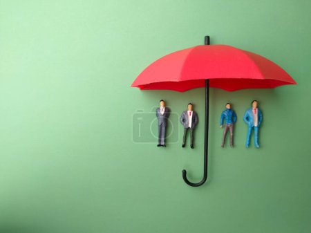 Foto de El paraguas rojo protegía a un hombre pequeño contra un fondo verde. El concepto de seguro de autoprotección. - Imagen libre de derechos