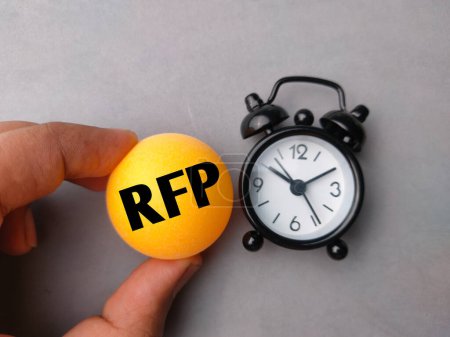 Téléchargez les photos : Main tenant balle de ping-pong et horloge avec mot RFP sur fond gris. - en image libre de droit