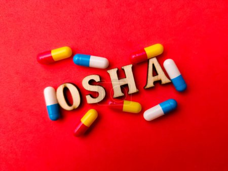 Téléchargez les photos : Pilule médicale avec mot en bois OSHA (Occupation Safety Health Administration) sur fond rouge. - en image libre de droit