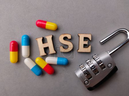 Téléchargez les photos : Cadenas et pilule médicale avec mot en bois HSE (Health Safety Environment) sur fond gris. - en image libre de droit