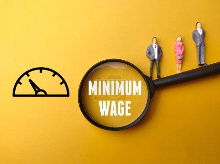 Miniature people, magnifying glass and icon with text MINIMUM WAGE on yellow background.