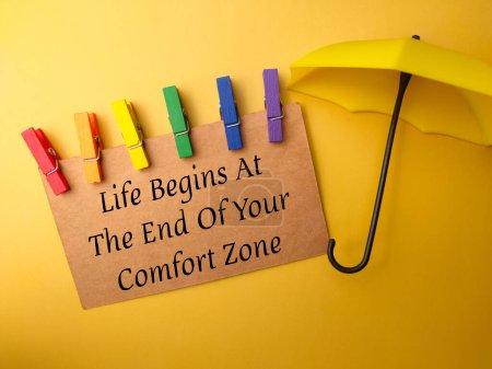 Photo for Umbrella and brown card with text Life Begins At The End Of Your Comfort Zone on yellow background. - Royalty Free Image