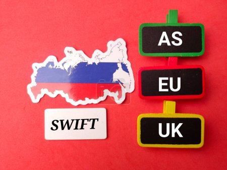 Vista superior Bandera de Rusia y tablero de madera con texto SWIFT AS EU UK sobre fondo rojo.