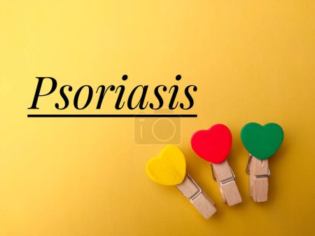 Draufsicht farbige Holzclips mit Text Psoriasis auf gelbem Hintergrund.