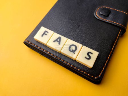 Foto de Juguetes palabra y cuaderno con texto FAQS sobre fondo amarillo. - Imagen libre de derechos
