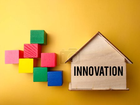 Top view wooden block andcwooden house with text INNOVATION on yellow background.