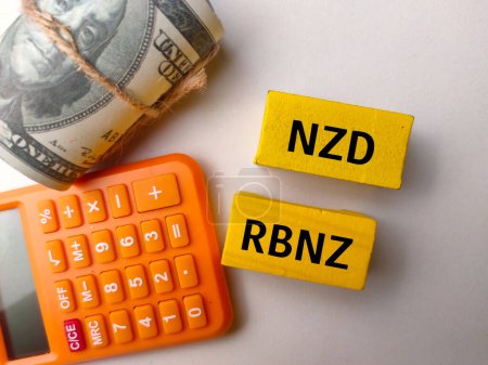 Calculadora de vista superior y billetes con texto NZD RBNZ sobre fondo blanco.