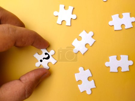 Photo for Top view hand holding white puzzle with symbol question mark on yellow background. - Royalty Free Image