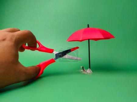 Jemand will einen roten Regenschirm mit roter Schere auf grünem Hintergrund schneiden