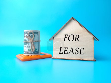 Banknotes,calculator and wooden house with text FOR LEASE on blue background.