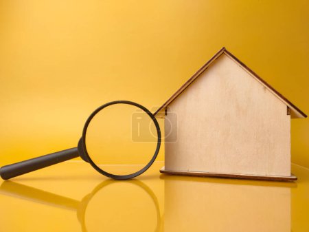 Wooden house and magnifying glass on a yellow background.