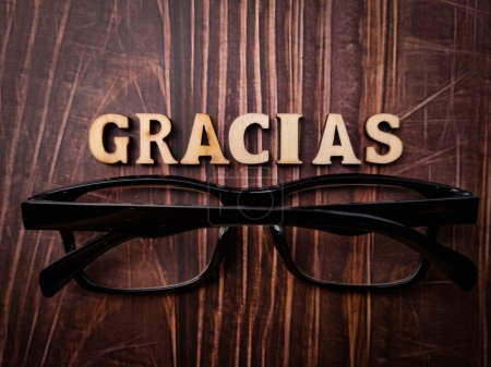 Top view glasses and wooden word with text GRACIAS on a wooden background.