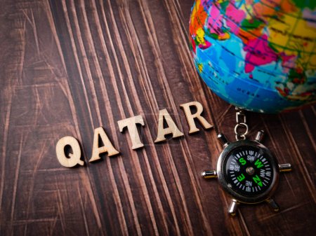 Top view compass,earth globe and wooden word with text QATAR on wooden background.