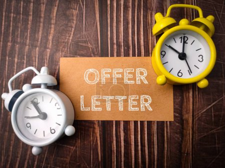Top view clock and brown card with text OFFER LETTER on wooden background.