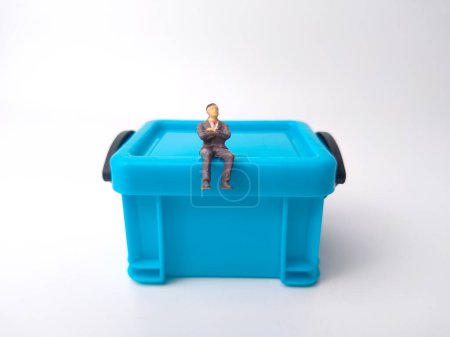 Foto de Personas en miniatura están sentadas en una caja de canasta de almacenamiento en miniatura azul sobre un fondo blanco - Imagen libre de derechos