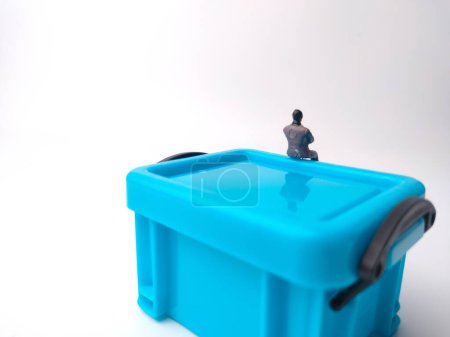 Foto de Personas en miniatura están sentadas en una caja de canasta de almacenamiento en miniatura azul sobre un fondo blanco - Imagen libre de derechos