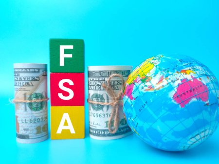 Earth globe and banknotes with word FSA on blue background.