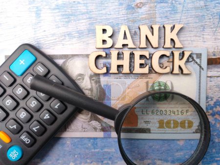 Banknoten von oben, Taschenrechner, Lupe und Holzwort mit Text BANK CHECK auf Holzgrund.