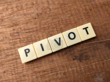 Top view toys word with text PIVOT on wooden background.