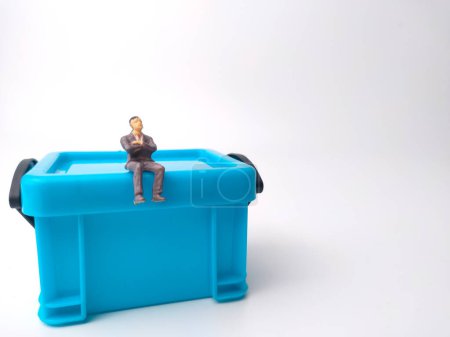 Foto de Personas en miniatura están sentadas en una caja de canasta de almacenamiento en miniatura azul sobre un fondo blanco con espacio de copia. - Imagen libre de derechos