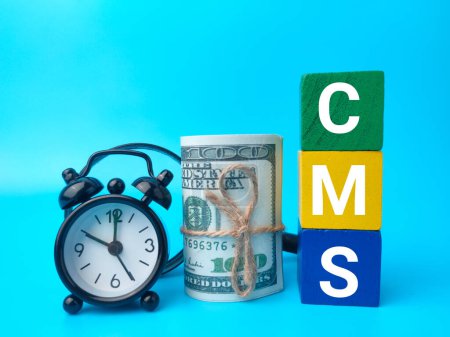 Foto de Billetes, reloj y cubo de madera con texto CMS sobre fondo azul. - Imagen libre de derechos