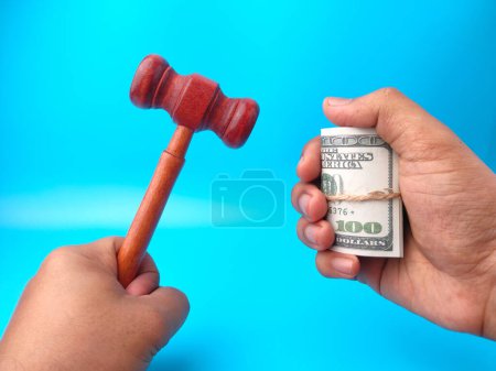 Hand holding gavel and banknotes on a blue background.