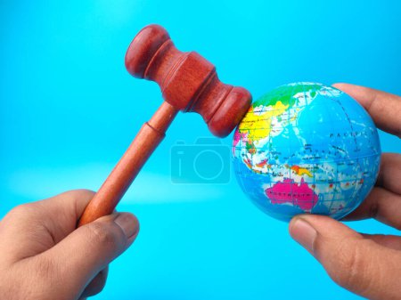 Mano sosteniendo martillo y globo terrestre sobre fondo azul. Concepto de derecho mundial.