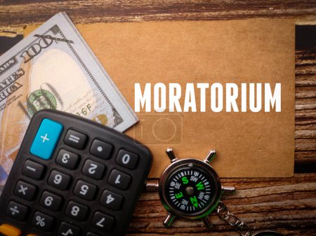 Top view calculator,compass and banknotes with text MORATORIUM on wooden background.