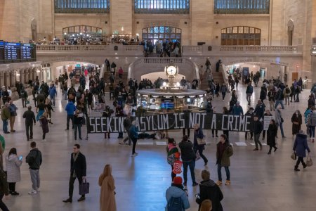 Téléchargez les photos : Manifestation pro-immigration à la gare Grand Central. 09 mars 2023, New York, New York, USA : Des gens traversent le Grand Central Terminal à Manhattan alors que des manifestants tenant des pancartes et des bannières se tiennent silencieusement pendant une manifestation - en image libre de droit