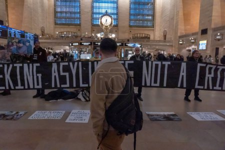 Photo for Pro-Immigration Demonstration In Grand Central Station. March 09, 2023, New York, New York, USA: People walk through Grand Central Terminal in Manhattan as protesters holding sign and banners stand silently during a protest - Royalty Free Image