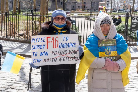 Téléchargez les photos : Cérémonie de levée de drapeau ukrainien. 19 mars 2023, New York, New York, États-Unis : Une femme tient une pancarte appelant à fournir du F16 à l'Ukraine lors d'une cérémonie de levée de drapeau ukrainien pour montrer sa solidarité avec le peuple ukrainien au parc historique Bowling Green - en image libre de droit