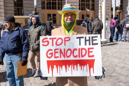 Photo for Ukrainian Flag Raising Ceremony. March 19, 2023, New York, New York, USA: A man holds a &quot;STOP THE GENOCIDE&quot; sign at a Ukrainian flag raising ceremony to show solidarity with the Ukrainian people at the historic Bowling Green Park - Royalty Free Image