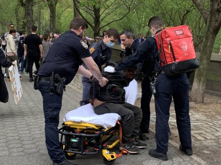 Foto de Un joven indigente atacó a una señora en Central Park. 16 de abril de 2023, Nueva York, Estados Unidos: Un joven sin hogar que estaba acostado en un asiento de hormigón en la 5ª Avenida con 67 calles de repente se levantó y atacó a una joven golpeándola - Imagen libre de derechos