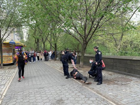 Foto de Un joven indigente atacó a una señora en Central Park. 16 de abril de 2023, Nueva York, Estados Unidos: Un joven sin hogar que estaba acostado en un asiento de hormigón en la 5ª Avenida con 67 calles de repente se levantó y atacó a una joven golpeándola - Imagen libre de derechos