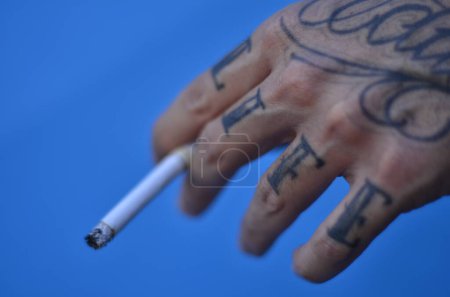 Photo for SUS offers treatment for smoking and nicotine addiction in Brazil. June 14, 2023. Natal, Rio Grande do Norte, Brazil: User smoking cigarette and having the word "LIFE" tattooed on his fingers, which means life. - Royalty Free Image