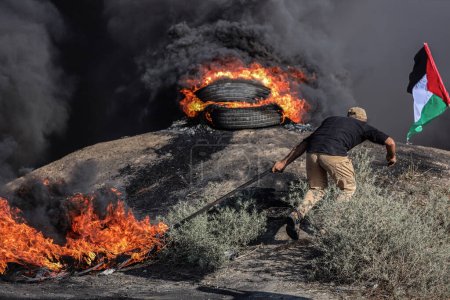 Foto de (INT) Jóvenes palestinos prendieron fuego a neumáticos de goma a lo largo de la frontera oriental de la Franja de Gaza. 3 de julio de 2023, Gaza, Palestina: Jóvenes palestinos queman neumáticos de goma en la frontera oriental de Gaza para expresar su ira - Imagen libre de derechos