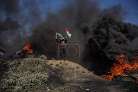 Foto de (INT) Jóvenes palestinos prendieron fuego a neumáticos de goma a lo largo de la frontera oriental de la Franja de Gaza. 3 de julio de 2023, Gaza, Palestina: Jóvenes palestinos queman neumáticos de goma en la frontera oriental de Gaza para expresar su ira - Imagen libre de derechos