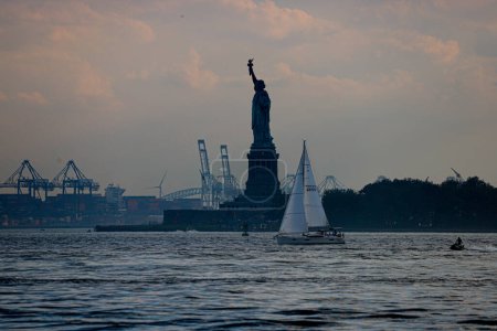 Téléchargez les photos : New York, USA - 07 / 03 / 2023 - CLIMAT / TRANSFERENCE / NEW YORK / USA - Statue de la Liberté sur Liberty Island et voilier dans le port de New York. Vue depuis Battery Park - en image libre de droit