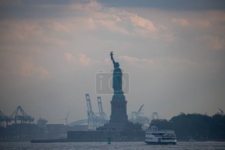 Téléchargez les photos : New York, USA - 07 / 03 / 2023 - CLIMAT / TRANSFERENCE / NEW YORK / USA - Statue de la Liberté sur Liberty Island et bateau dans le port de New York. Vue depuis Battery Park - en image libre de droit