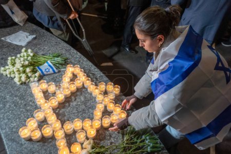 Téléchargez les photos : Eric Adams, maire de New York, organise une veillée aux chandelles pour les victimes d'attentats terroristes en Israël. 9 octobre 2023, New York, New York, USA : Une femme drapée du drapeau israélien s'occupe du mémorial improvisé fait de bougies commémoratives - en image libre de droit