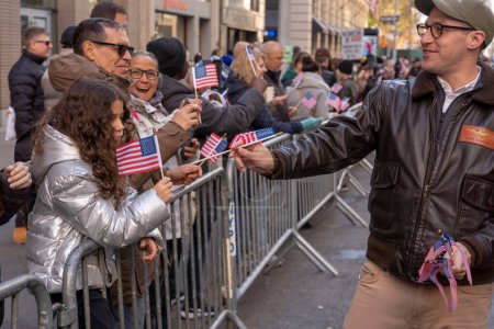 Photo for Veteran's Day Parade Held In New York City. November 11, 2023, New York, New York, USA: A participant hands out flag to spectators in the annual Veterans Day Parade on November 11, 2023 in New York City. Hundreds of people lined 5th Avenue - Royalty Free Image