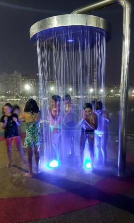 Foto de SANTOS (SP), Brasil 28 / 12 / 2023 - La fuerte ola de calor a principios del verano ha llevado a turistas y residentes de la costa de Sao Paulo a acudir a las playas. Este jueves (28), los niños prefirieron prolongar sus baños en la ducha - Imagen libre de derechos