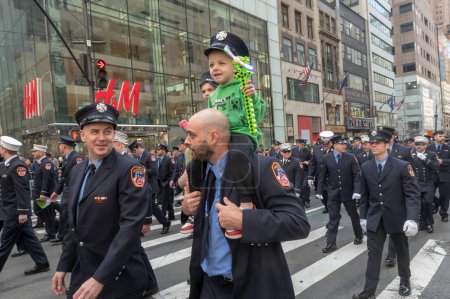 Foto de Desfile del Día de San Patricio en la ciudad de Nueva York. 16 de marzo de 2024, Nueva York, Nueva York, Estados Unidos: Un miembro de la ciudad de Nueva York. Departamento de Bomberos marcha con un niño en su hombro - Imagen libre de derechos