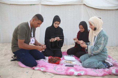 Foto de El equipo de voluntarios de Gaza entretiene a los niños con Qatar. 28 de marzo de 2024, Khan Yunis, Gaza, Palestina: Un evento organizado por el Equipo de Voluntarios de Gaza en el Mar de Mawasi en Khan Yunis para hacer Qatayef y entretener a los niños - Imagen libre de derechos